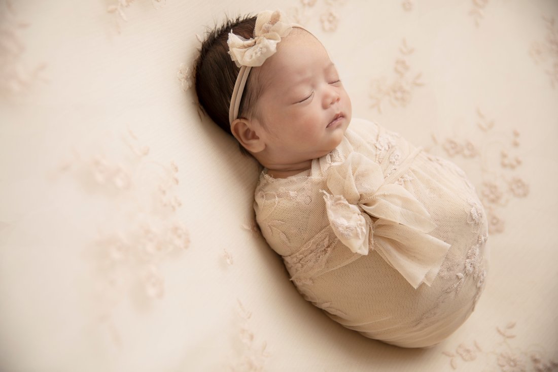 Newborn girl swaddled in ivory lace, sleeping peacefully